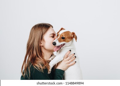 Leuke jonge vrouw kust en knuffelt haar puppy jack russell terrier hond. Liefde tussen baas en hond. Geïsoleerd op een witte achtergrond. Studioportret.