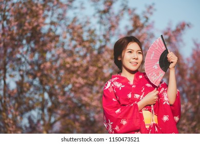 桜の花を背景に着物と赤い扇子を持つアジアの女性