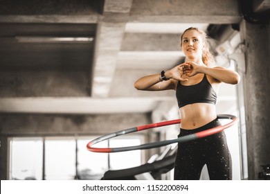 Schöne kaukasische junge Frau, die Hula Hoop in Schritt Taille Reifen vorwärts Haltung tut. Junge Frau, die Hula Hoop während einer Übungsklasse in einer Turnhalle tut. Gesunder Sportlebensstil, Fitness, gesundes Konzept.