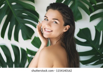 Retrato de mujer joven y hermosa con piel suave perfecta en hojas tropicales. Concepto de cosmética natural y cuidado de la piel.
