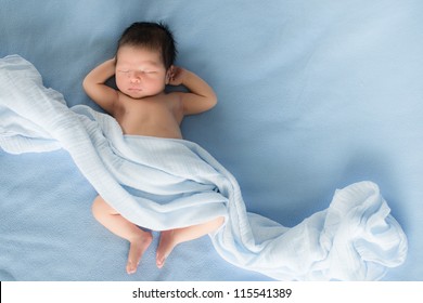 Pasgeboren 4 dagen oude babyjongen liggend op zijn rug ontspannen onder een blauwe wikkeldoek