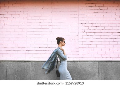 Chụp Phong Cách Đường Phố Của Người Phụ Nữ Trên Bức Tường Màu Hồng. Cô gái Swag mặc áo khoác jean, váy xám, đeo kính râm. Phong cách sống thời trang ngoài trời