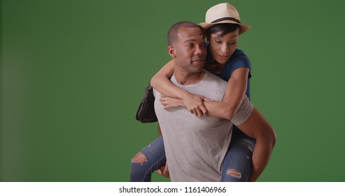 En sort mand giver kæresten piggy back ride på grøn skærm
