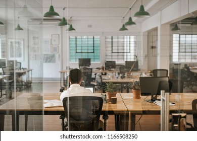 Rearview of a young businessman sitting alone at his desk in an office working on a laptop and going over paperwork
