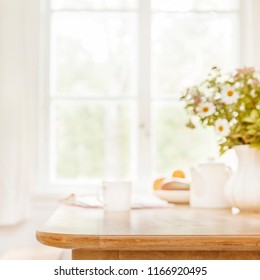 Huis houten keukentafelblad met focus vooraan en onscherpe achtergrond met ontbijttafelkleding, raamkozijn en een vaas gevuld met tuinbloemen. Ruimte voor tekst.