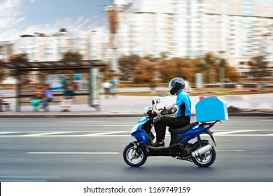 Elviteles ételt kézbesítő fiú robogón, csomagtartós dobozzal gyorsan vezet sietségben. Futár szállít ételt robogóval, hogy elkerülje a dugókat.