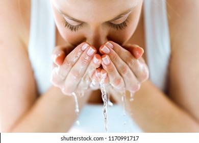 Retrato de una hermosa joven lavándose la cara salpicando agua en un baño de casa.