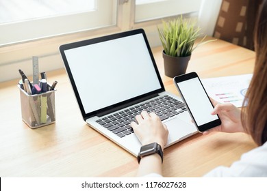 mujer sosteniendo un teléfono inteligente y usando una computadora portátil en la mesa en la sala de oficina en ventanas con árboles y fondo natural, para montaje de visualización de gráficos. Aprovecha tu pantalla para poner publicidad.