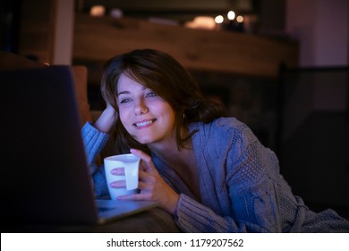 Mujer muy sonriente viendo una película en su computadora portátil en casa.