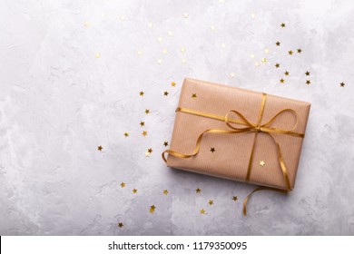 Kotak hadiah yang dibungkus kertas kerajinan dengan pita emas dan bintang di atas batu abu-abu