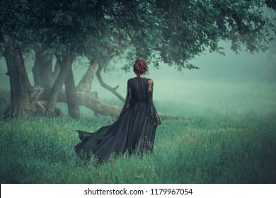 Fantasy Ghost Girl Walk dunkle Natur Wald lange schwarze Vintage Kleid Zug winken Fliegenwind. Art Gothic Königin Hexe. Baumnebel. Kunstwerk mysteriöse Silhouette schöne junge Frau mittelalterliche Seidenkleider