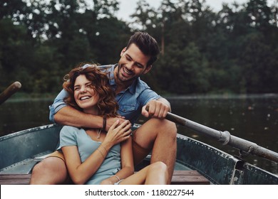 Getting away from everything. Beautiful young couple embracing and looking away while enjoying romantic date on the lake       
