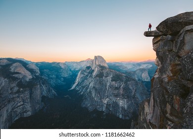 Een onverschrokken wandelaar staat op een overhangende rots en geniet van het uitzicht op de beroemde Half Dome op Glacier Point, over het hoofd gezien in de prachtige avondschemering, Yosemite National Park, Californië, VS
