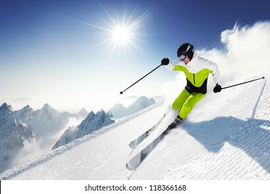 Esquiador en montaña, pista preparada y día soleado.
