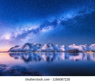 Helle Milchstraße über schneebedeckten Bergen und Meer in der Nacht im Winter in Norwegen. Landschaft mit schneebedeckten Felsen, Sternenhimmel, Spiegelung im Wasser, Fjord. Lofoten. Raum. Schöne Milchstraße