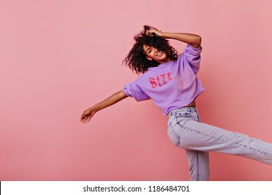 Schöne wohlgeformte Frau, die mit inspiriertem Gesichtsausdruck tanzt. Debonair schwarzes Mädchen im purpurroten Hemd, das auf rosigem Hintergrund lächelt.