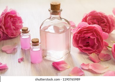 Rose oil in glass bottles with bright pink flowers on white wooden background, SPA concept