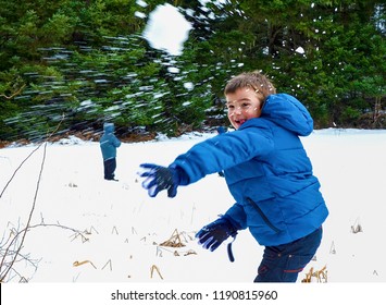 Boy in blue warm coat having fun in beautiful winter place with snowballs