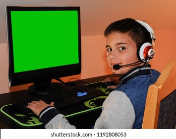 ヘッドフォンとカラフルなキーボードを身に着けているコンピューターでビデオゲームをプレイする若いゲーマーの少年