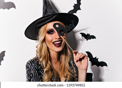 Joyful european woman playfully posing in halloween. Adorable young witch with black makeup expressing happiness.
