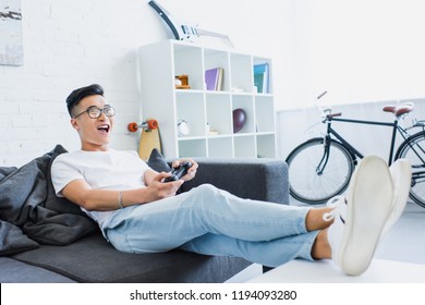 opgewonden knappe aziatische man die een videogame speelt op de bank in de woonkamer
