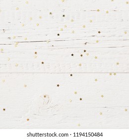 Closeup of small golden stars confetti on old white wooden background. Holiday and celebration concept