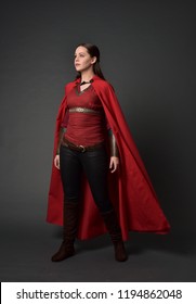 full length portrait of brunette girl wearing red medieval costume and cloak. standing pose on grey studio background.
