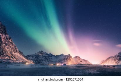 Borealra cực quang xanh và tím trên núi tuyết. Đèn phương Bắc ở đảo Lofoten, Na Uy. Bầu trời đầy sao với đèn vùng cực. Cảnh quan về đêm mùa đông với cực quang, đá cao, bãi biển. Đi du lịch. Phong cảnh