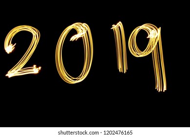 Lichtmalerei Fotografie, Langzeitbelichtung, goldmetallisches gelbes Licht, das die Ziffern '2019' vor einem schwarzen Hintergrund buchstabiert. Frohes neues Jahr Konzept