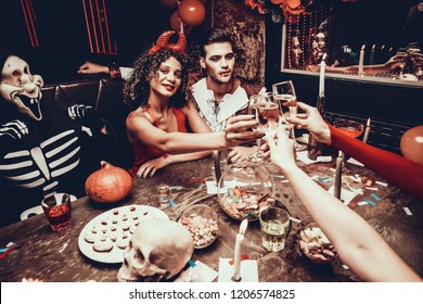 Jonge lachende mensen in kostuums rammelende glazen. Groep jonge gelukkige mensen die kostuums dragen op Halloween-feest aan tafel zitten en champagne drinken. Viering van Halloween