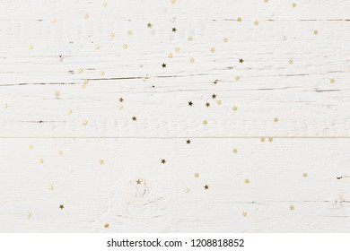 Top view on small golden stars confetti on old white wooden background.