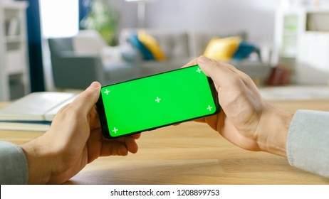 First Person Close-up of the Man Holding Green Screen Smartphone in Landscape Mode and Playing in a Racing Video Game by Tilting Mobile Phone. Background Cozy Living Room.