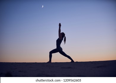 Schéin jonk Fra praktizéiert Yoga Asana Virabhadrasana 1 - Krieger Pose 1 an der Wüst an der Nuecht