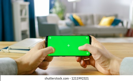 First Person Close-up of the Man Holding Green Screen Smartphone in Landscape Mode and Playing Game with His Thumbs.