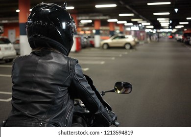 Isoleret bagfra af kvindelig motorcyklist, der kører en tohjulet sportscykel langs underjordisk pakingparti gang, og parkerer sin motorcykel efter nattur. Motorcykling, ekstremsport og livsstil