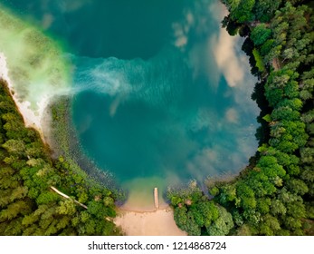 Aerial top down view of beautiful green waters of lake Gela. Birds eye view of scenic emerald lake surrounded by pine forests. Clouds reflecting in Gela lake, near Vilnius city, Lithuania.