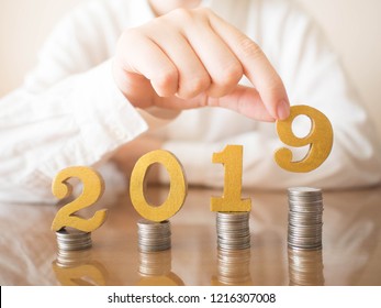 2019 New year saving money and financial planning concept. Female hands putting gold wooden number 2019 on stack of coins. Creative idea for business growth, tax payment, investment and banking.