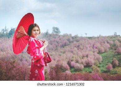 桜の花を背景に着物と赤い和傘を着けたアジアの女性