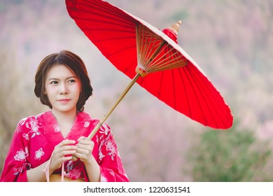 桜の花を背景に着物と赤い和傘を着けたアジアの女性