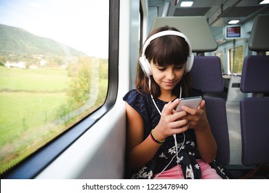電車で旅行中に彼女のスマート フォンを使用してヘッドフォンで幸せな少女