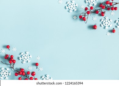Composición navideña o invernal. Marco hecho de copos de nieve y bayas rojas sobre fondo azul pastel. Navidad, invierno, concepto de año nuevo. Plano, vista superior, espacio de copia
