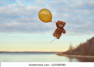 Teddybär fliegt mit einem großen gelben Ballon in den Himmel. Ein Bär fliegt über den See. Winnie Pooh fliegt mit Ballon.