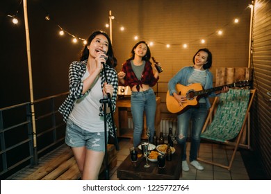 屋上で曲を練習する音楽を演奏するバンド。若い女の子は、夜の屋上で屋外のカラオケ パーティーで音楽を楽しむのが大好きです。快適なデスクチェアの横のテーブルに食べ物やアルコール飲料。