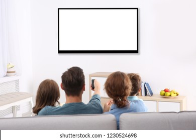 Familie med fjernbetjening, der sidder i sofaen og ser tv derhjemme, plads til design på skærmen. Fritid og underholdning