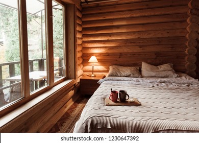Rustic interior of log cabin bedroom. Cozy bed by big window. Breakfast on a tray in hotel.