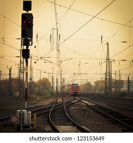 Moble photography lo-fi styled image of a red commuter train on an urban railway track with confusing lines and overhead cables and a red signal light