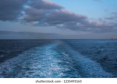 View of the water trail in the ocean of the departing vessel against the background of the horizon and clouds