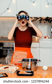 mladá surprsied hospodyňka drží bonocular při vaření vánoční večeře v kuchyni v červené zástěře.