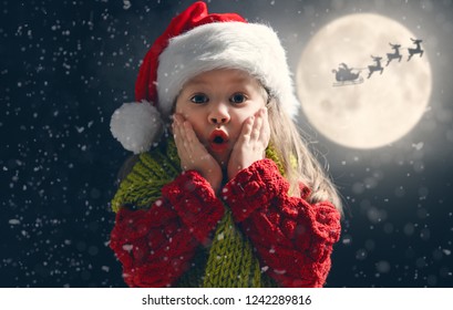 Đứa trẻ dễ thương vào Giáng sinh. Ông già Noel bay trên chiếc xe trượt tuyết của mình trên bầu trời mặt trăng. Bé vui vẻ tận hưởng kỳ nghỉ. Chân dung của cô gái với những món quà trên nền tối.