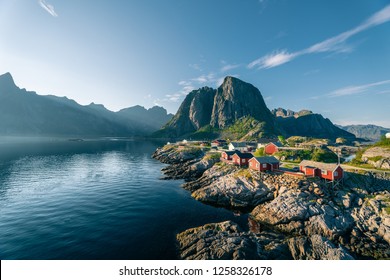 Cabañas rojas de rorbu junto a un océano en calma en la soleada tarde de verano en las islas Lofoten, Reine, Noruega